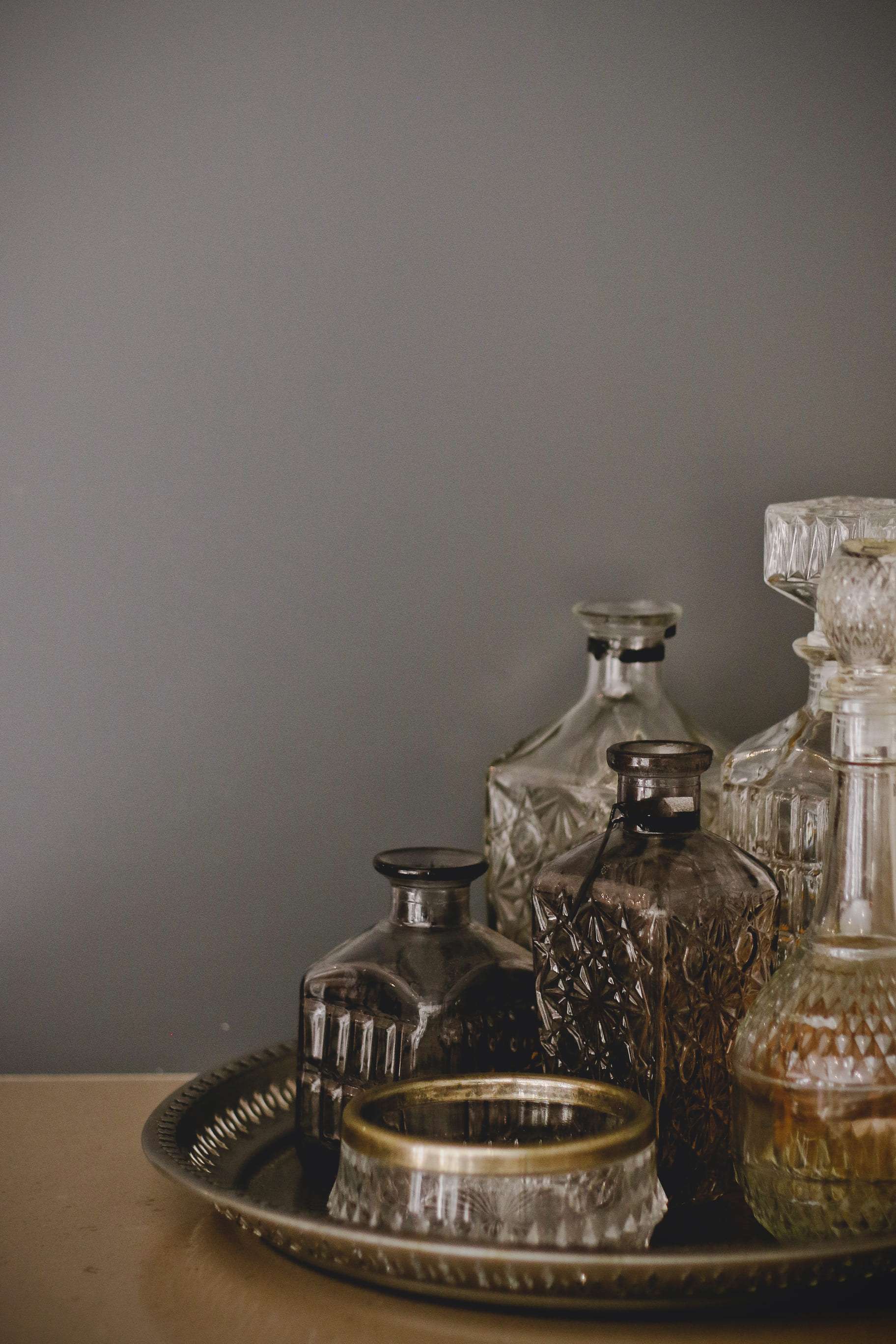 Detail photo of various empty glass bottles and decanters in a round metal tray against a wall as part of a project by Lace Interiors